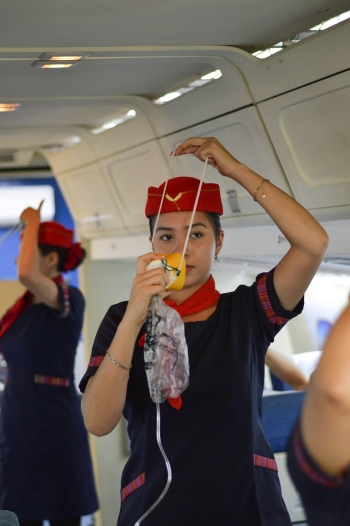 Flight attendant shows how to put on your oxygen mask.